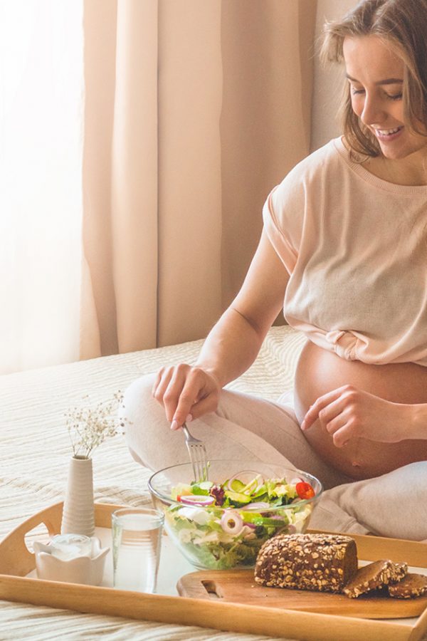 Pregnancy and healthy organic nutrition. Pregnant woman enjoying fresh vegetable salad in bed, free space. Concept of expectation and health.